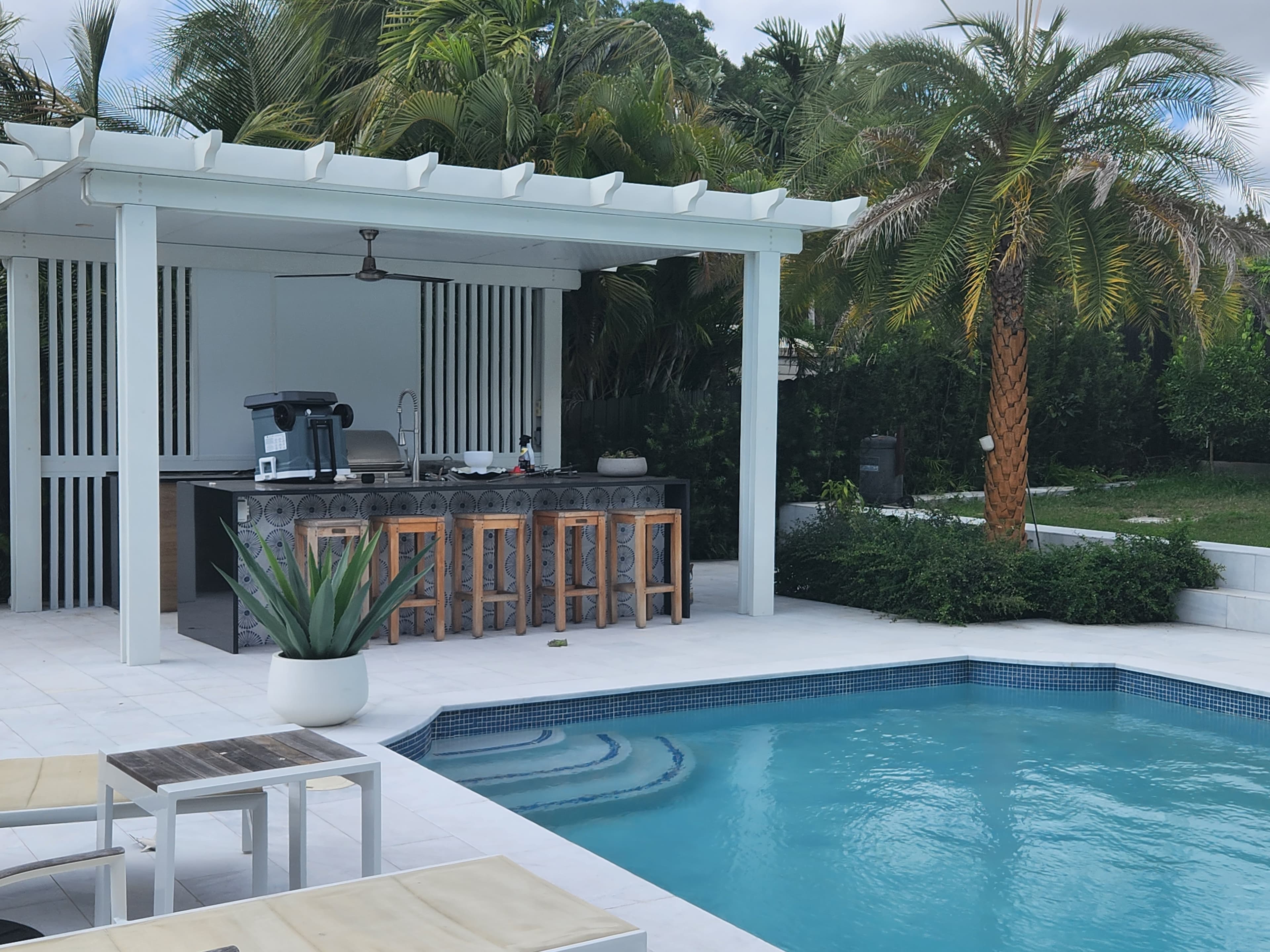 Pérgola de aluminio blanco con barra de cocina de exterior junto a la piscina